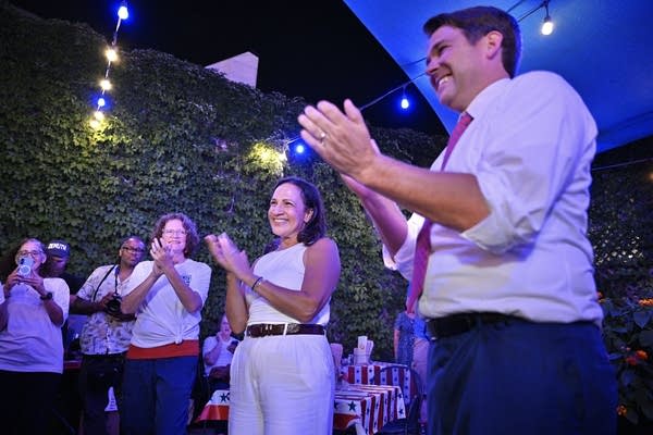 A woman in white and a man in a white shirt and red tie applaud.