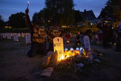 People kneel at a replica of a gravestone during twilight. 