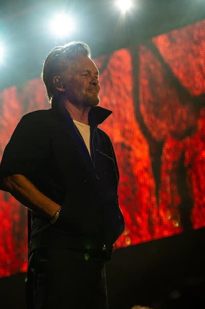 A musician with hands in his coat pockets smiles at a large audience