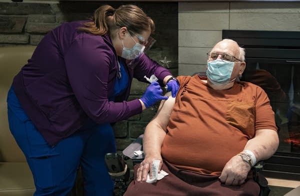 An older man sitting in a wheelchair gets a shot. 