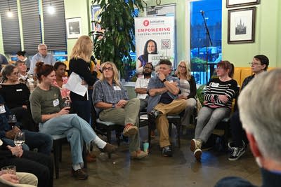 People sit in a space in the restaurant as one woman stands holding a microphone.