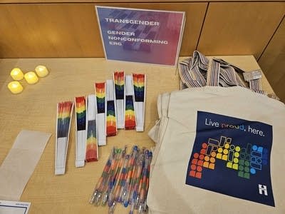 Rainbow-patterned freebies are laid out on a table, including fans, pens and tote bags.