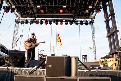 A musician sings and plays guitar on an outdoor stage