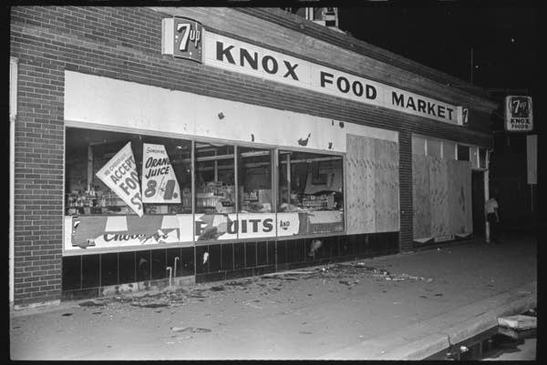 Black and white, a broken storefront at night lit by flash. 