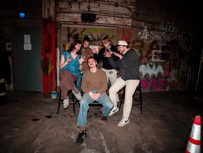 Five musicians sit on stools in a garage.