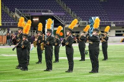 A marching band performs on the field of a football stadium.