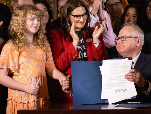 A young girl holds hands with the governor after a bill is signed