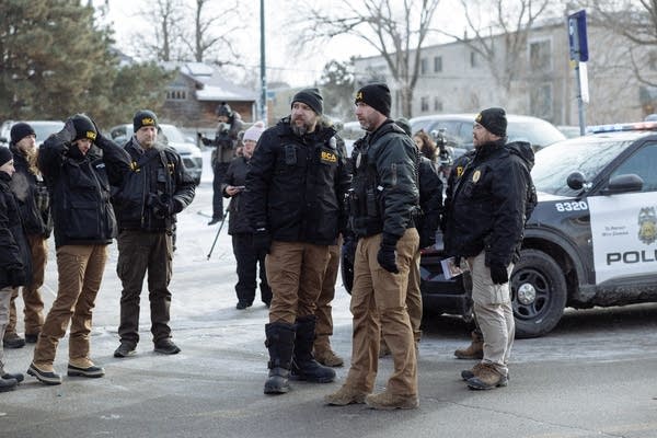 BCA agents and police officers gather near squad cars.