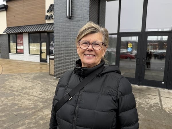 A woman in a black winter coat poses for a photo in front of a store.