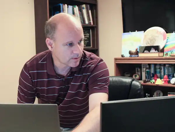 A man in a striped shirt operates a laptop.