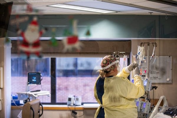 A nurse wearing PPE checks an IV in a patient's hospital room. 