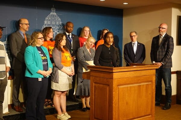 A group of people stand behind a podium to speak to reporters.