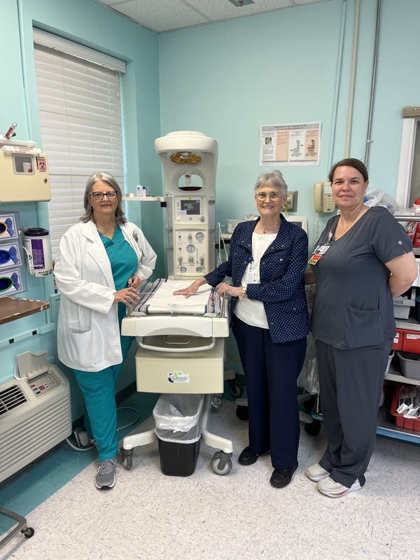 Three health care providers pose for a photograph in the nursery at the D.W. McMillan Memorial Hospital.