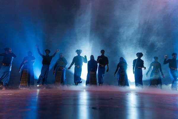 Performers emerge through smoke on to a stage.