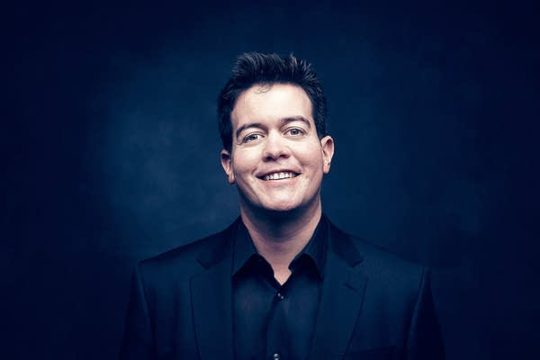 A man in a collared shirt and blazer poses for a studio portrait