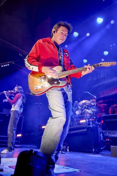 A musician plays guitar onstage in a large music venue