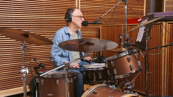 A musician sings and plays drums in a recording studio