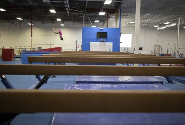 A teen flips as she dismounts from a balance beam. 