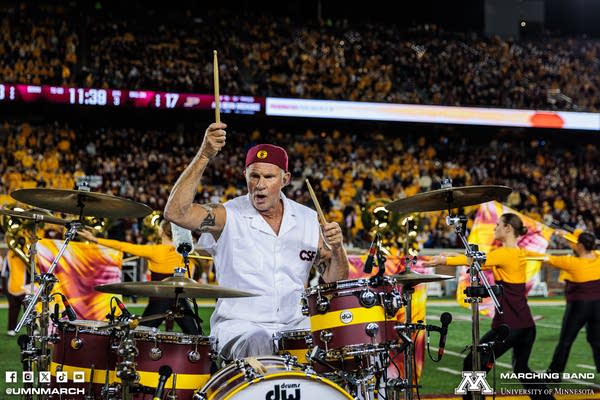 A musician plays drums as a marching band perform with him