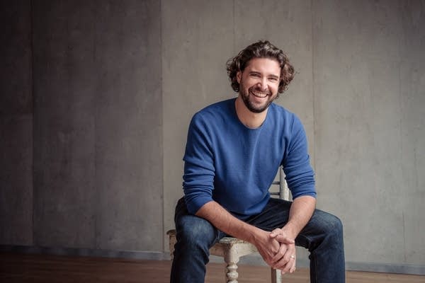 A man in casual clothes smiles for a studio portrait