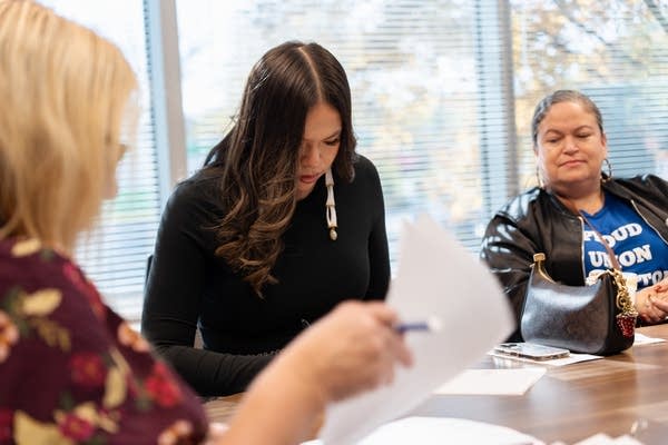 Three women at a conference table review a document.