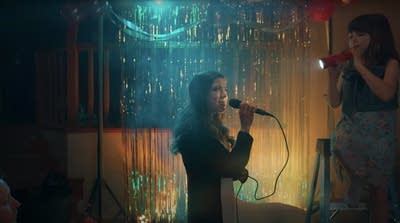 A woman sings into a karaoke microphone while a child shines a light on her