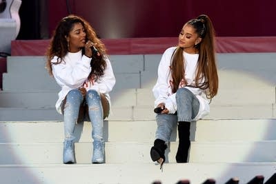 Two women sit next to one another onstage, singing together
