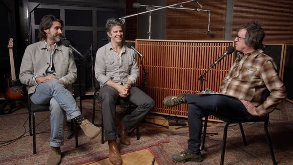Three men have a conversation in a recording studio
