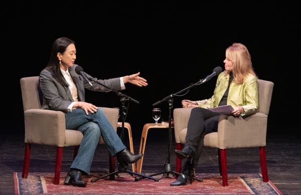 Two people sit on a stage with microphones.