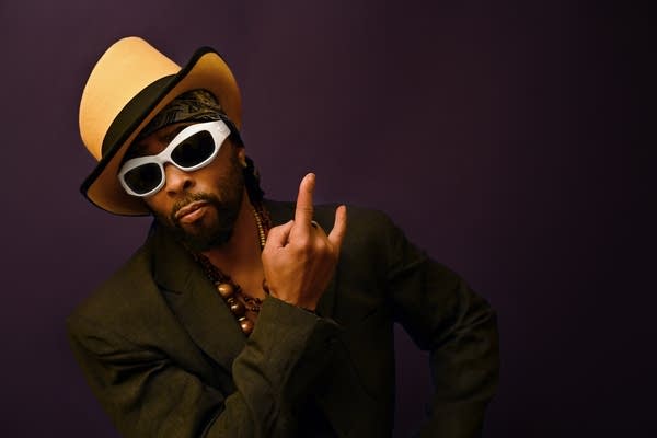 A man wears sunglasses, a hat, and stylish attire.