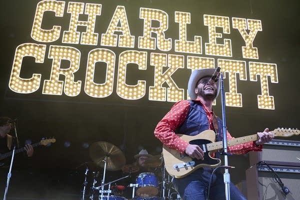 A man in a cowboy hat performs onstage under a bright lighted letters installation
