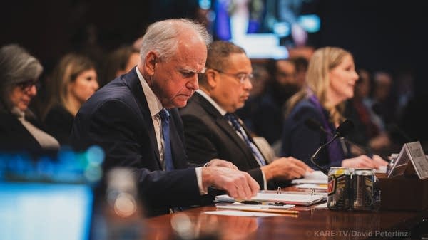 Three people sit at a hearing.