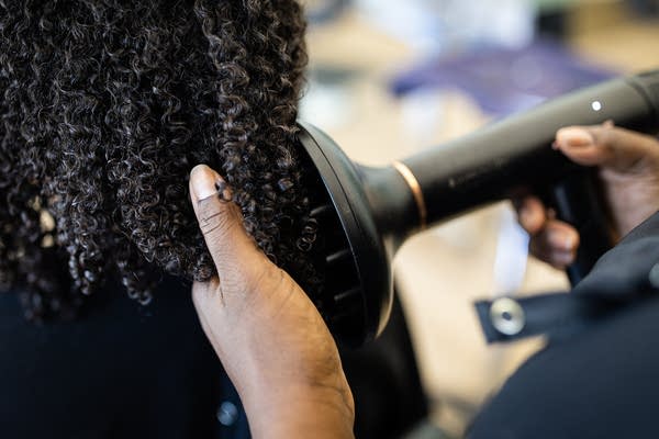 A Black woman styles a woman's hair