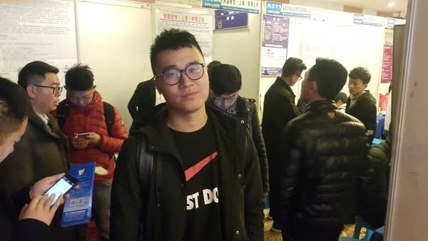 A man in glasses stand in a crowded job fair.
