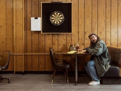 Dan Hornsby wears a baseball cap and barn jacket. He is sitting in a booth.