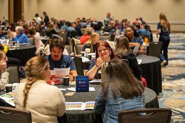 Groups of people sit at round tables in a conference room.