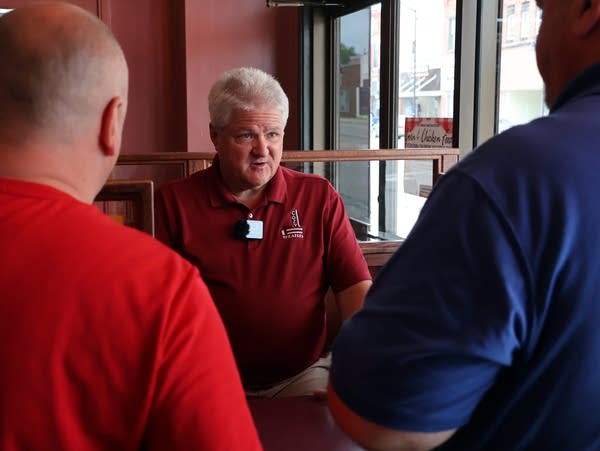 a man in a red shirt talks to to men 