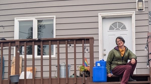 Caitlin Lenahan with blue water jugs on the porch of her "dry cabin" near Fairbanks, Alaska.
