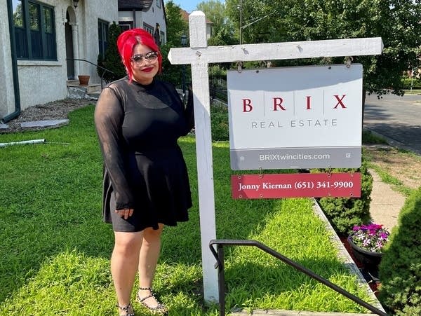 Person stands next to real estate sign