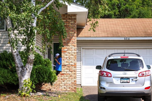 A person outside of a house with a car in front of it