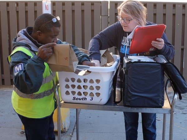 Two people arrange a basket filled with paper sacks.