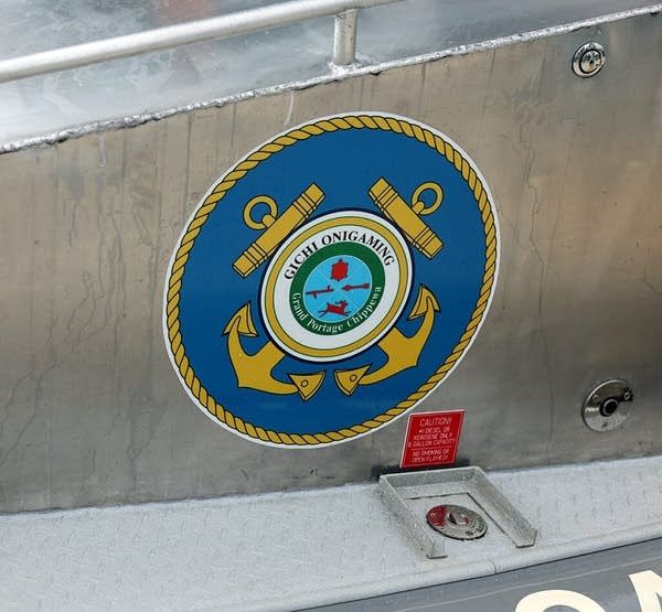 A marine seal with yellow anchors crossed on a blue circle. It reads, "Gichi Onigaming, Grand Portage Chippewa."