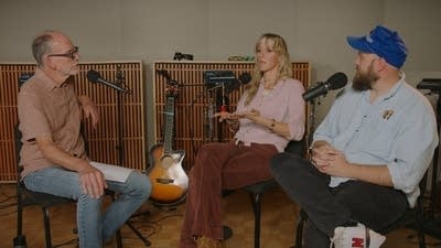 Three people have a conversation in a recording studio