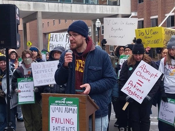 Man speaking at podium with signs in background