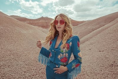 A woman in a tailored suit and sunglasses standing in an arid canyon