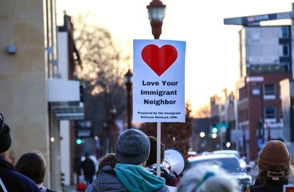 A sign with a red heart that reads, "Love Your Immigrant Neighbor."