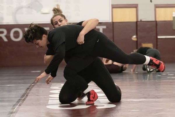 Two people wrestling on a mat in a gym.