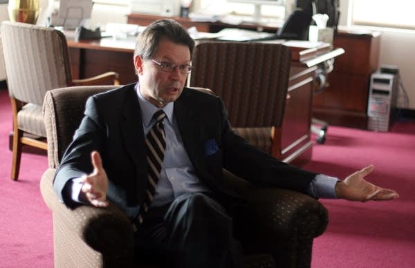 A man in a suit sits in an office chair.