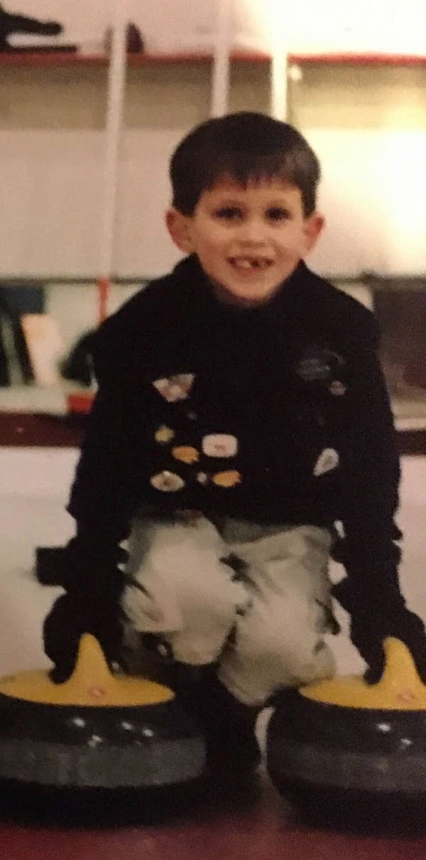 A young boy poses next to two curling stones.