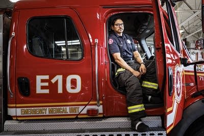 A firefighter sits in the cab of a fire engine with the door open.